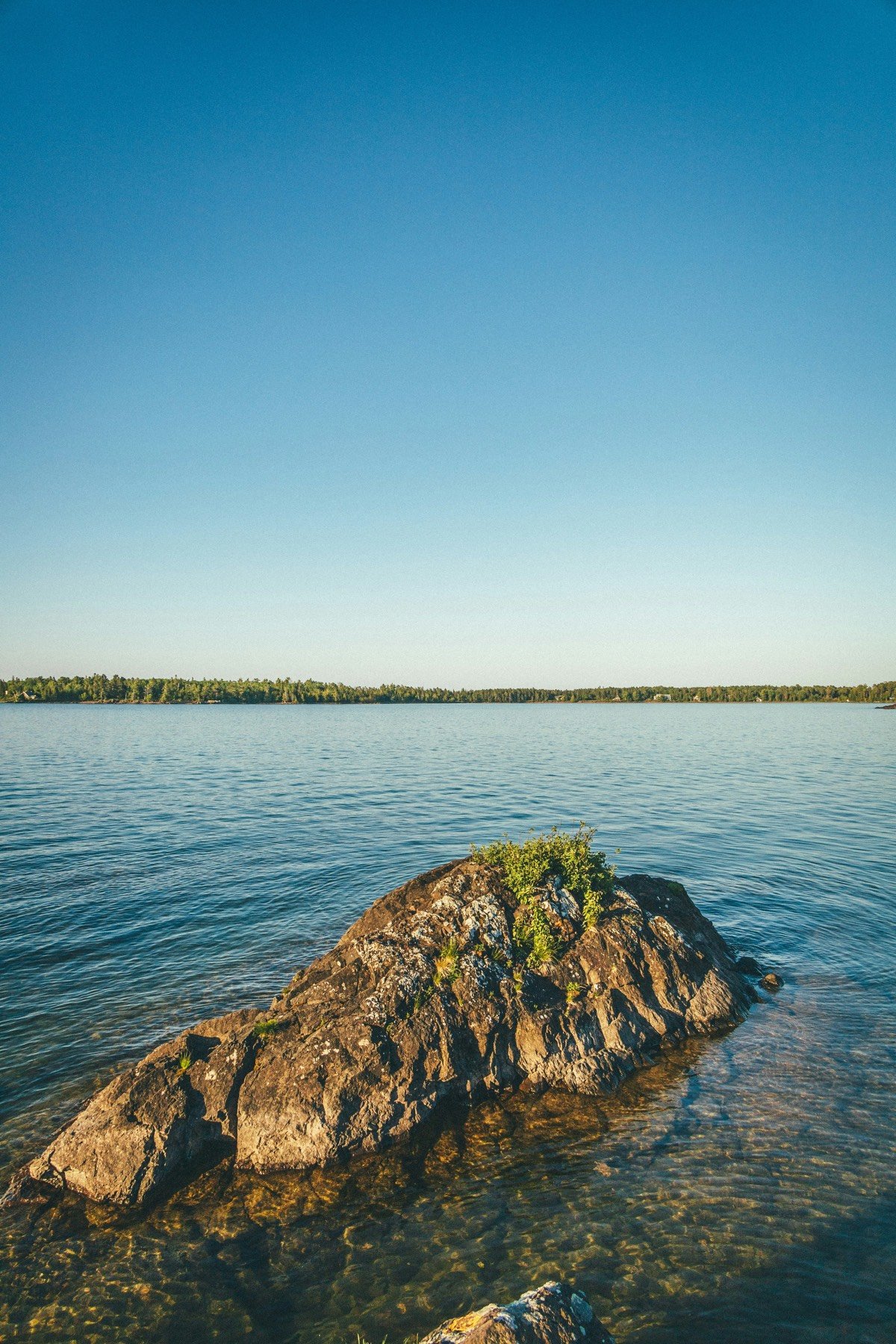 Sunlit rocks beside a calm lake and wooded shoreline